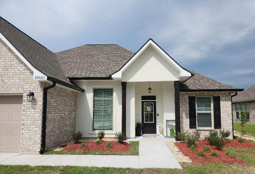 A picture of the front of a house with white stucco, bricks  and black gutters in covington, LA
